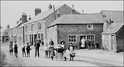 Street scene from about 1905.  In the background, Eben Taylor stands at the doorway of his cobbler's business