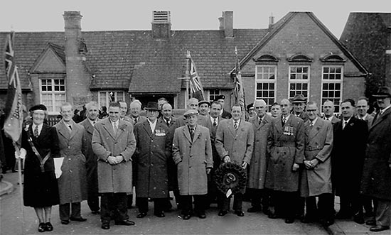 Members gathered for Remembrance Day parade c1950s with the Mission Room in the background.  L-R: Josie Crick, Mr T Hawkins, Mr A Buckby, Mr W Taylor, Mr Phillips, Mr F T Peck (President), Mr J Bull, Mr F Wells (almost hidden), Mr Prested, Mr J Blott (mostly hidden by Mr W T Brace Snr), Mr H Sawyer, Mr A Caffrey, ? standard bearer, Mr W A Brace Jnr, Dennis Crick (Legion Standard Bearer), Mr E Watson, Mr J Edwards, Mr A Byland, ?, ?, Mr L Blowfield, Mr F Pentelow, Mr H Dicks, Mr G Ward